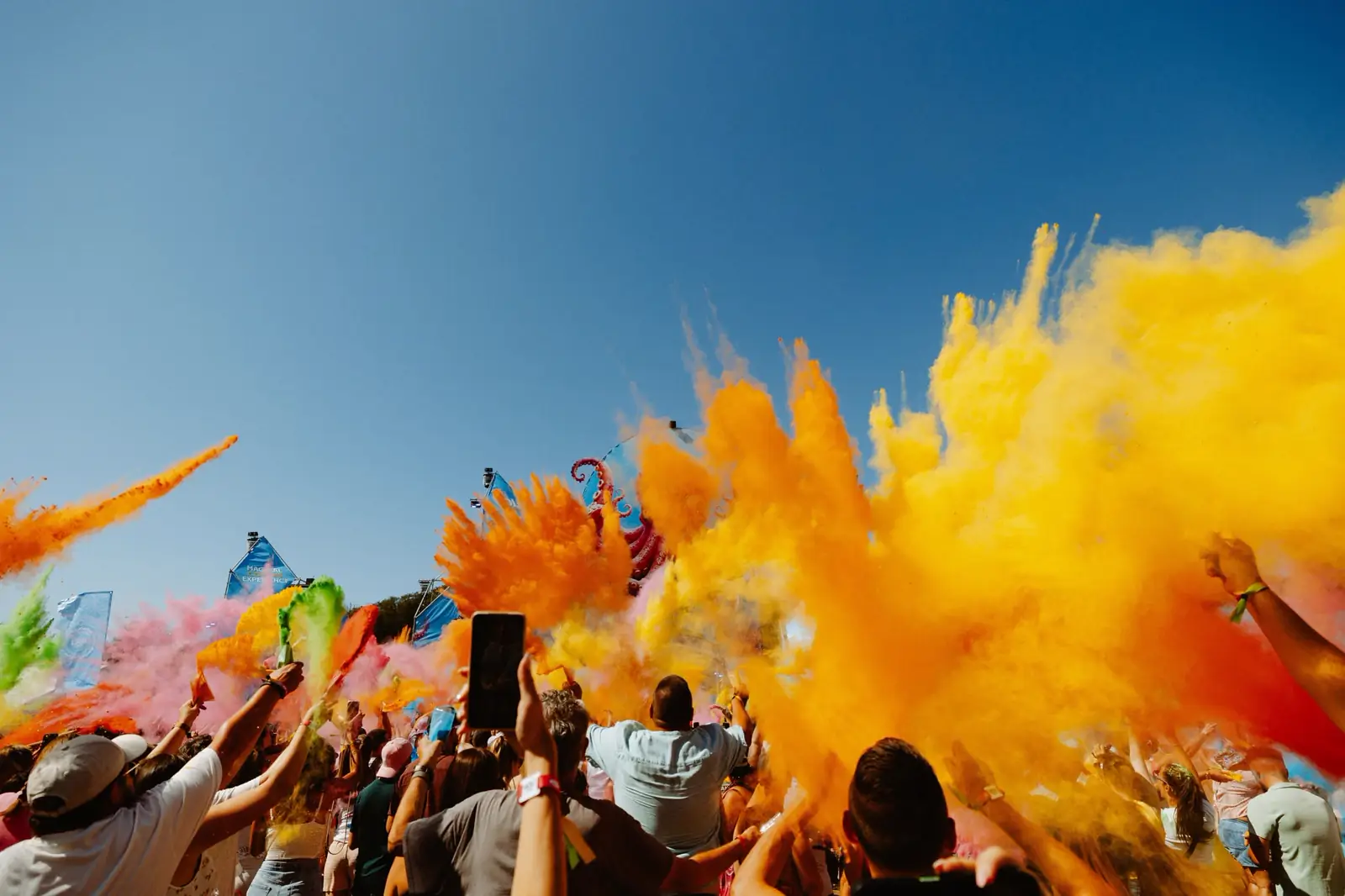 Explosion de poudre orange et jaune au-dessus de la foule, sous le ciel bleu du festival